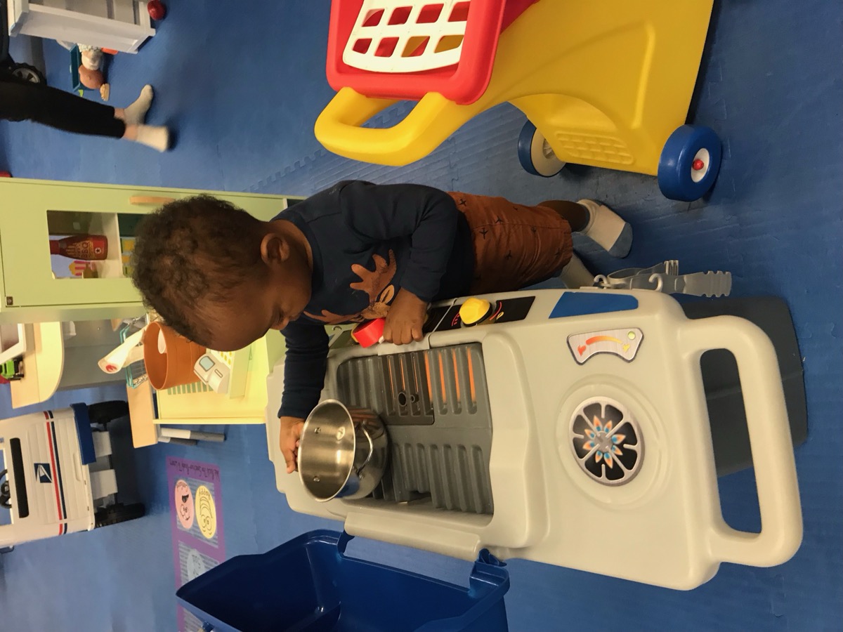 Toddler Yohannes standing at a toy kitchen play set, pretending to cook with a small pot