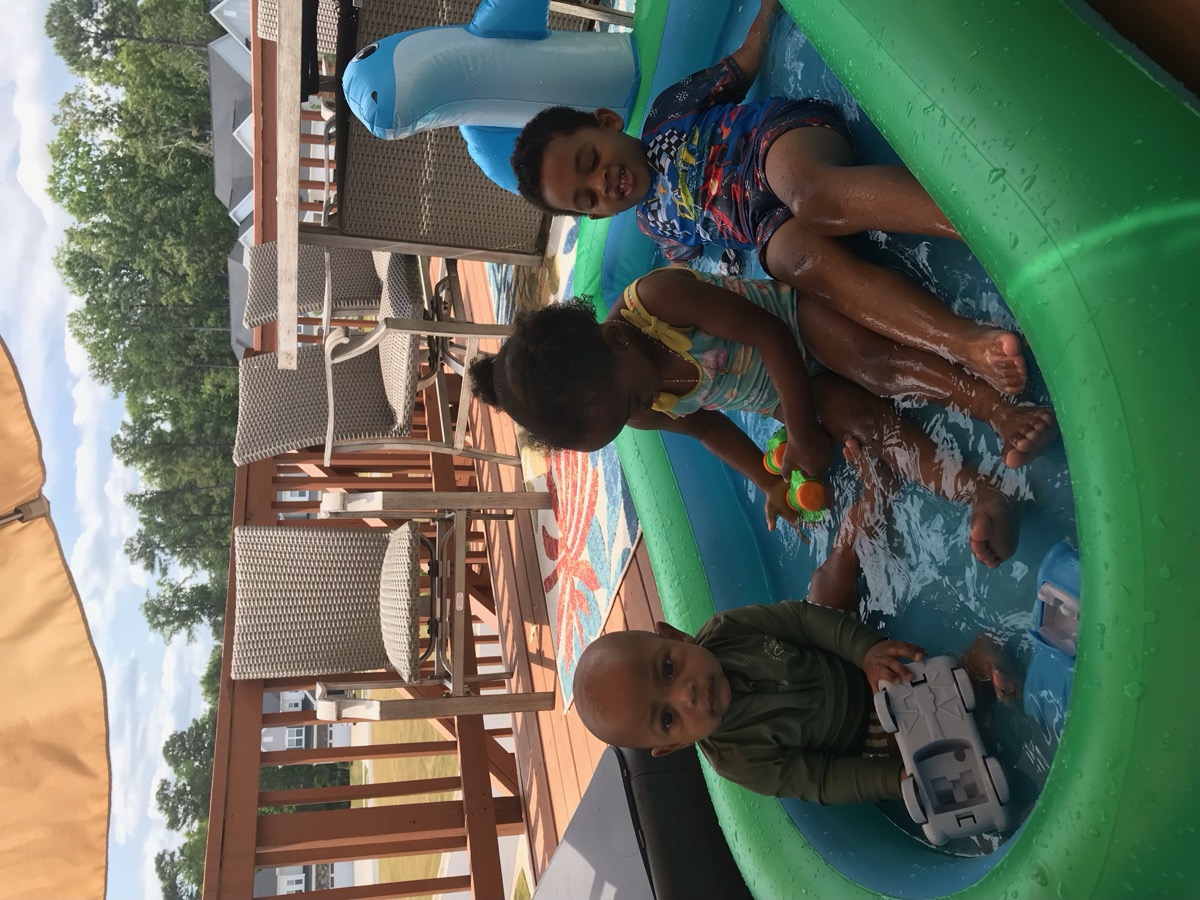All three siblings splashing in a green inflatable pool on the back deck on a summer day