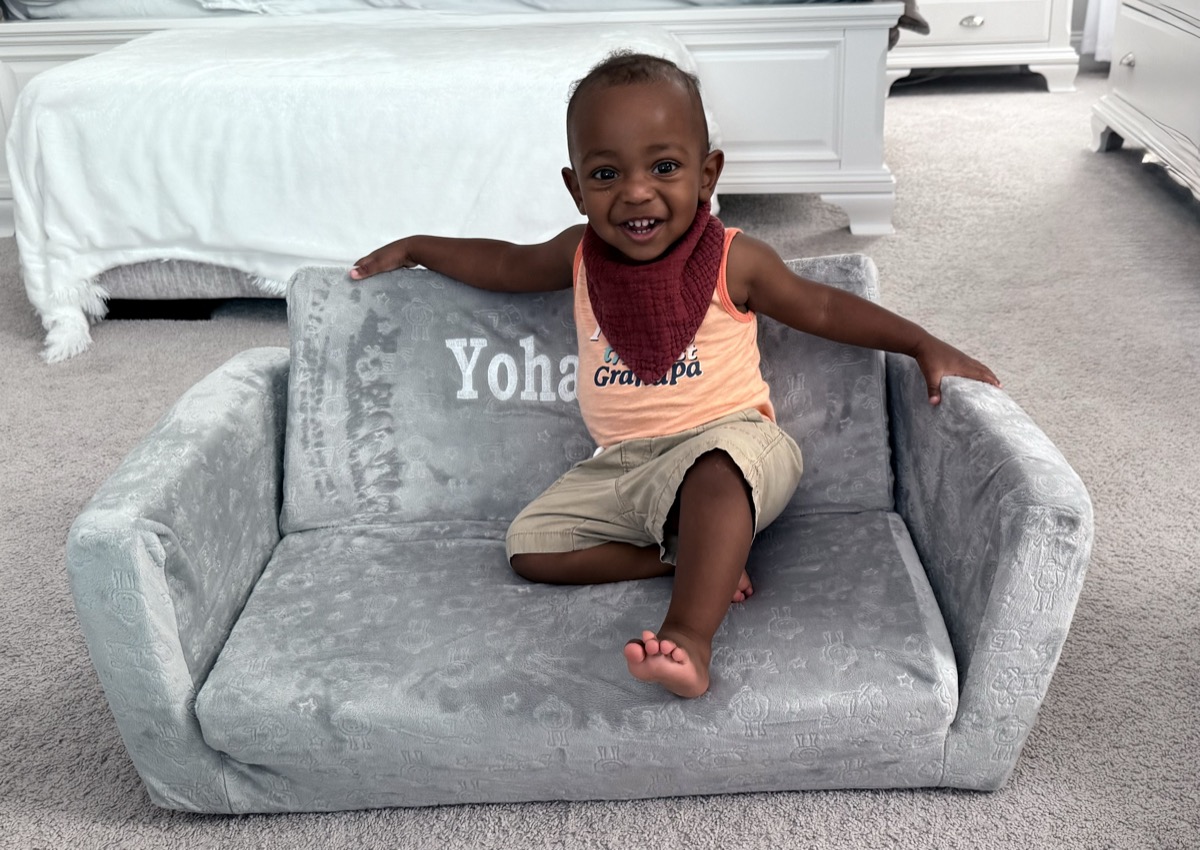 Yohannes sitting on his personalized gray toddler couch embroidered with his name, wearing an orange Grandpa tank top and a burgundy bandana bib