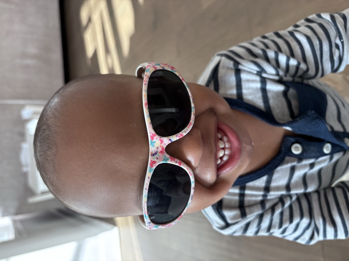 Close-up of baby Yohannes grinning ear to ear in floral-print sunglasses and a striped henley shirt